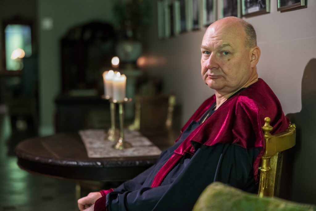 vyras su tamsiu apsiaustu ziuri i kamera