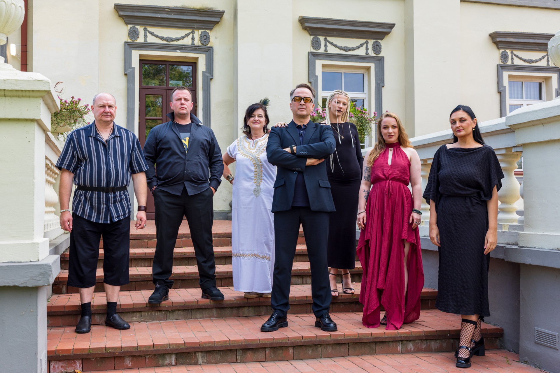 vyrai ir moteris stovi ant laiptu prie dvaro ir ziuri i kamera